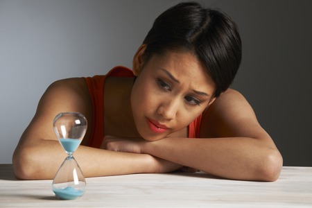 Sad Young Woman Looking At Hourglass