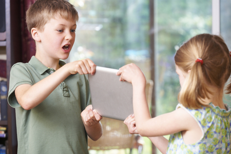 Boy And Girl Fighting Over Digital Tablet At Homeの写真素材