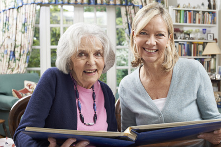 Senior Woman Looks At Photo Album With Mature Female Neighborの写真素材