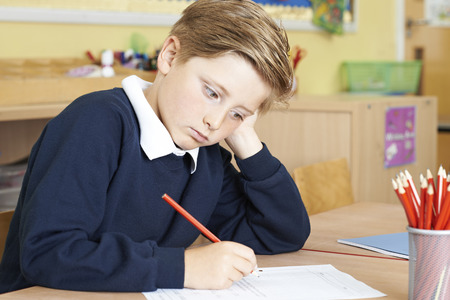 Bored Male Elementary School Pupil At Deskの写真素材
