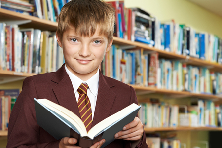 Boy Wearing School Uniform Reading Book In Libraryの写真素材