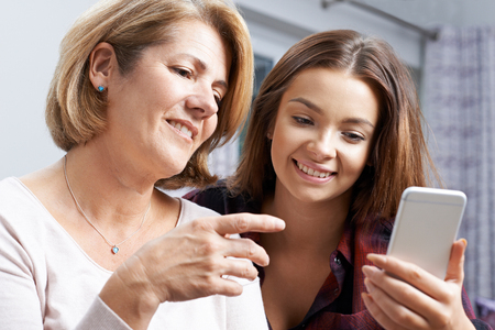 Teenage Daughter Showing Mother How To Use Mobile Phoneの写真素材