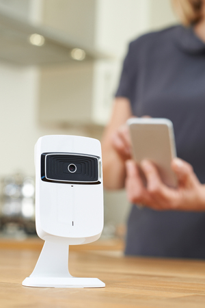 Woman Controlling Smart Security Camera Using App On Mobile Phoneの写真素材