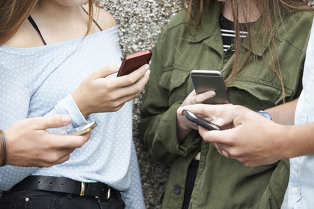 Group Of Teenagers Sharing Text Message On Mobile Phonesの写真素材
