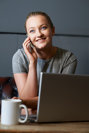 Businesswoman Talking On Mobile Phone Working On Laptop In Internet Cafeの写真素材