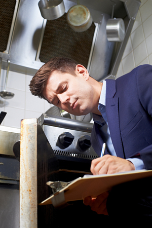 Health Inspector Looking At Oven In Commercial Kitchenの写真素材