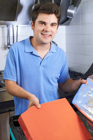 Portrait Of Pizza Delivery Person Putting Food Into Insulated Bag In Restaurant Kitchenの写真素材