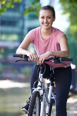 Young Woman Cycling Next To River In Urban Settingの写真素材