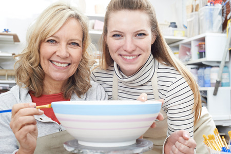 Portrait Of Mature Woman Decorating Bowl With Teacher In Pottery Classの写真素材