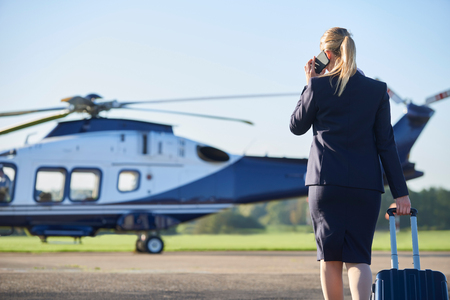 Rear View Of Businesswoman Walking Towards Helicopter Whilst Talking On Mobile Phoneの写真素材