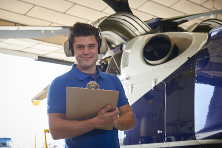 Portrait Of Male Aero Engineer With Clipboard Carrying Out Check On Helicopter In Hangarの写真素材