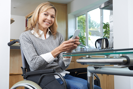 Portrait Of Disabled Woman In Wheelchair Using Mobile Phone At Homeの写真素材