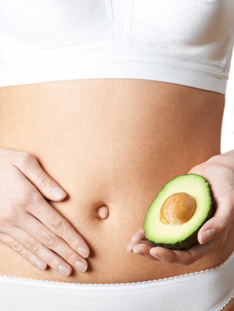 Close Up Of Woman In Underwear Holding Avocado And Touching Stomachの写真素材