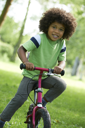 Young Boy Learning To Ride Bike In Parkの写真素材