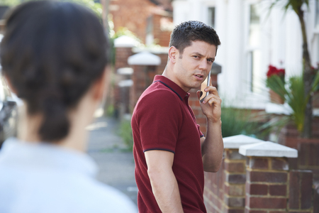 Man Calling For Help On Mobile Phone Whilst Being Stalked On City Street By Womanの写真素材