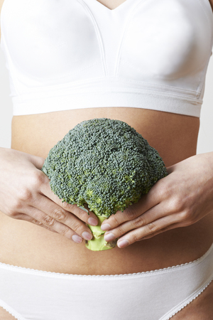Close Up Of Woman In Underwear Holding Bunch Of Broccoli And Touching Stomachの写真素材