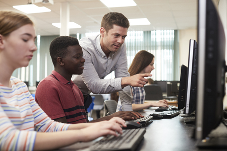 Teacher Helping Male High School Student Working In Computer Classの写真素材