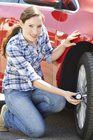 Portrait Of Woman Checking Car Tyre Pressure Using Gaugeの写真素材