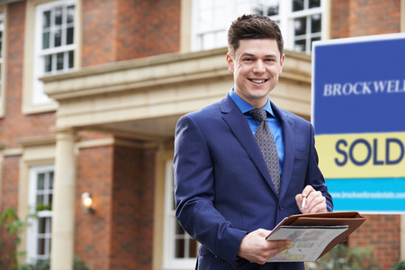 Portrait Of Male Realtor Standing Outside Residential Property With Sold Signの写真素材