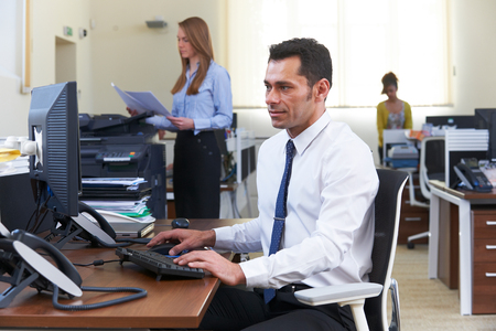 Businessman Working At Desk In Busy Officeの写真素材