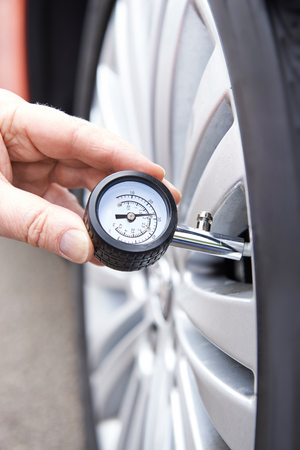 Close-Up Of Man Checking Car Tyre Pressure With Gaugeの写真素材