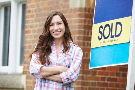 Smiling Woman Standing Outside New Home With Sold Signの写真素材
