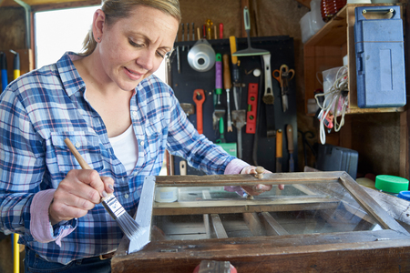 Mature Woman Upcycling Furniture In Workshop At Home  Painting Cabinetの写真素材