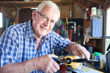 Portrait Of Senior Man Working On Model Radio Controlled Aeroplane In Shed At Homeの写真素材