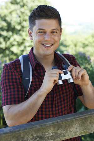 Portrait Of Young Man Hiking In Countryside Looking Through Binocularsの写真素材