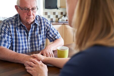 Woman Talking With Unhappy Senior Man Sitting In Kitchen At Homeの写真素材