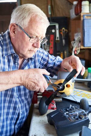 Senior Man Working On Model Radio Controlled Aeroplane In Shed At Homeの写真素材