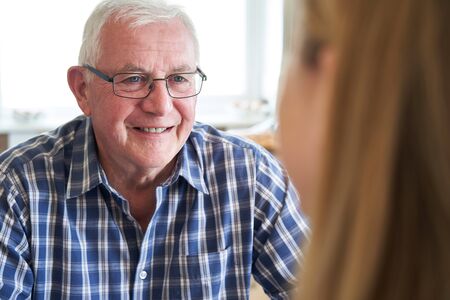 Smiling Senior Man Sitting In Kitchen Talking With Woman At Homeの写真素材