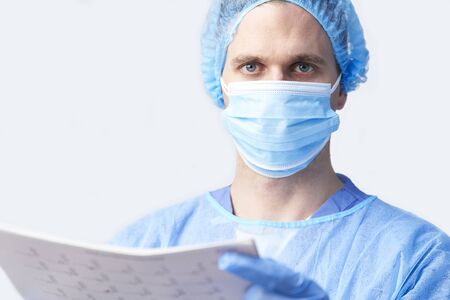 Studio Portrait Of Male Surgeon Wearing Gown And Mask Holding Medical Print Outの写真素材