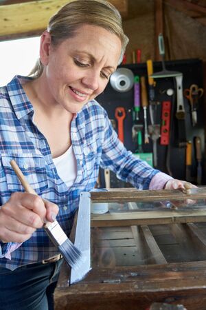 Mature Woman Upcycling Furniture In Workshop At Home Painting Cabinetの写真素材