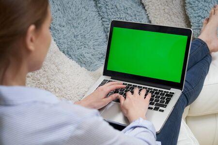 Over The Shoulder View Of Woman Lying On Sofa Using Green Screen Laptopの写真素材