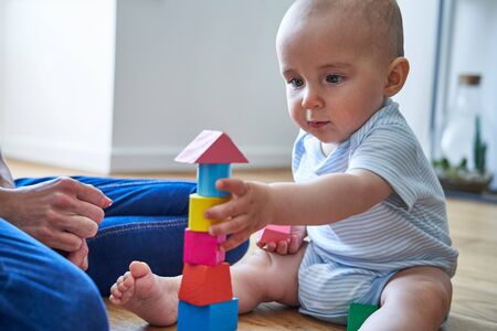 Mother With 8 Month Old Baby Son Learning Through Playing With Coloured Wooden Blocks At Homeの写真素材