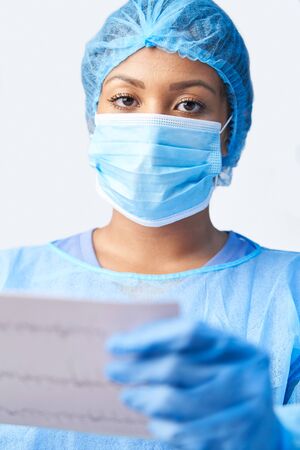 Studio Portrait Of Female Surgeon Wearing Gown And Mask Holding Medical Print Outの写真素材