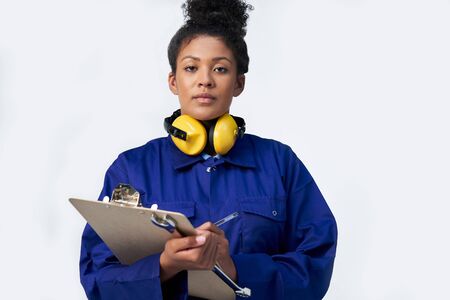 Portrait Of Studio Shot Of Female Engineer With Clipboard And Spanner Against White Backgroundの写真素材