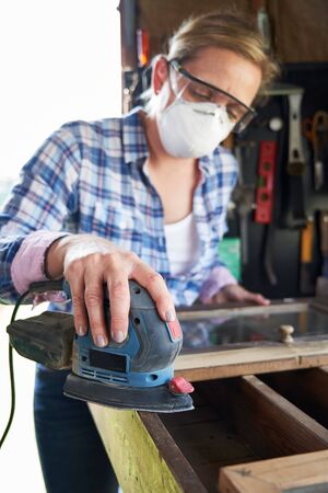 Mature Woman Upcycling Furniture In Workshop At Home Using Electric Sanderの写真素材