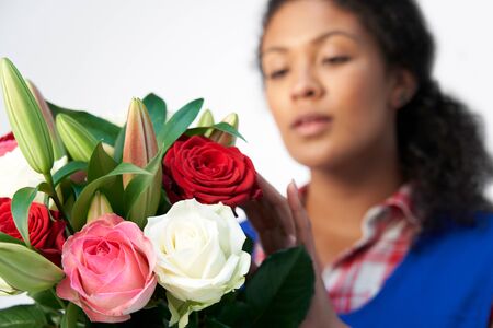 Studio Shot Of Female Florist Arranging Bouquet Of Lillies And Roses Against White Backgroundの写真素材