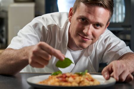 Portrait Of Male Chef Garnishing Plate Of Food In Professional Kitchenの写真素材