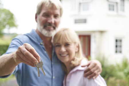 Portrait Of Mature Couple Standing In Garden In Front Of Dream Home In Countryside Holding Keys