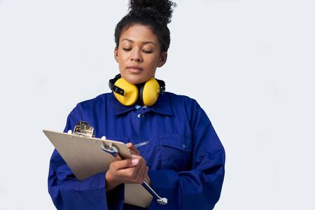 Studio Shot Of Female Engineer With Clipboard And Spanner Against White Backgroundの写真素材