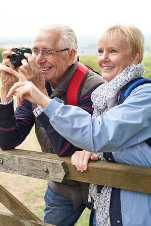 Senior Couple Hiking In Countryside Standing By Gate  And Taking Photo With Cameraの写真素材
