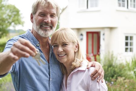 Portrait Of Mature Couple Standing In Garden In Front Of Dream Home In Countryside Holding Keysの写真素材