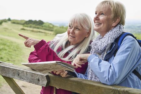 Two Senior Women Friends On Walking Holiday Resting On Gate With Mapの写真素材
