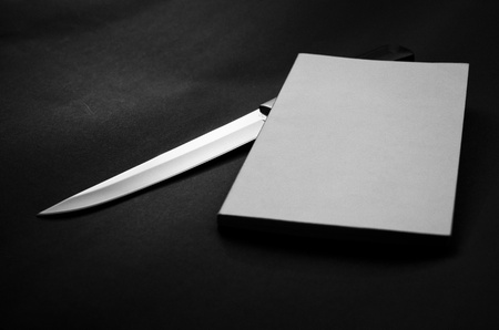 Sharp knife and a blank book cover in black and white.