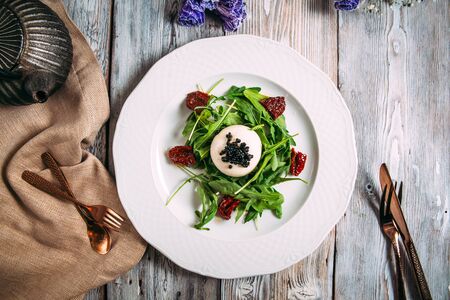 Top view on a gourmet salad with mozzarella caviar sun-dried tomatoes on a white plate on the wooden table, horizontal formatの写真素材