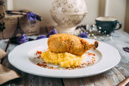 Appetizing deep fried chicken leg on mashed potatoes on a white plate on the wooden table, horizontal formatの写真素材