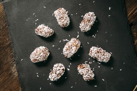 Sweet appetizing chocolate sweets candies in coconut flakes on the balck background, horizontal